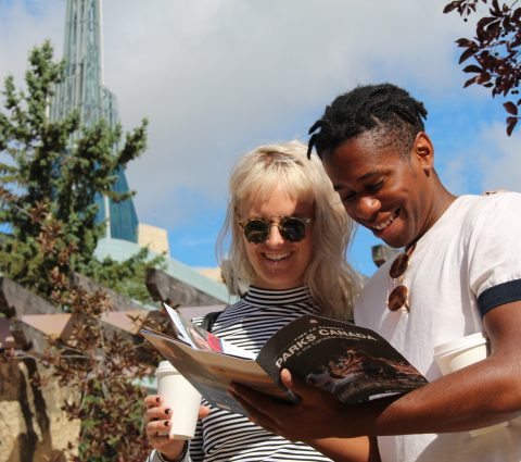 Besucher lesen eine Broschüre von Parks Canada an der The Forks National Historic Site.