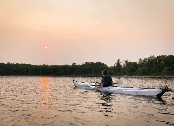 A person in a kayak on Lake William looking up at a red sun