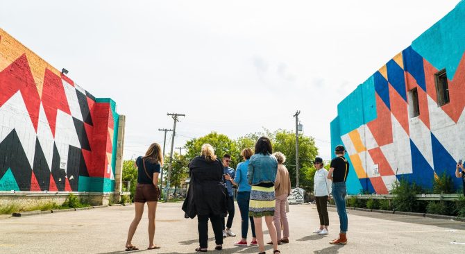 Un grupo de personas se encuentra en un claro pavimentado entre dos edificios con coloridos murales de mantas de estrellas.