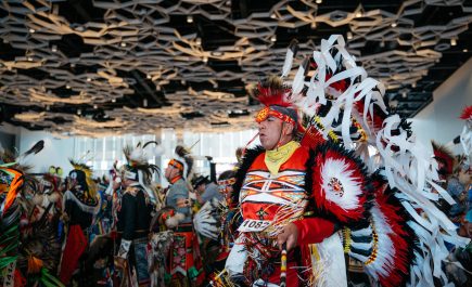 Une personne autochtone portant une coiffe traditionnelle danse avec d'autres personnes lors du pow-wow du festival Manito Ahbee.