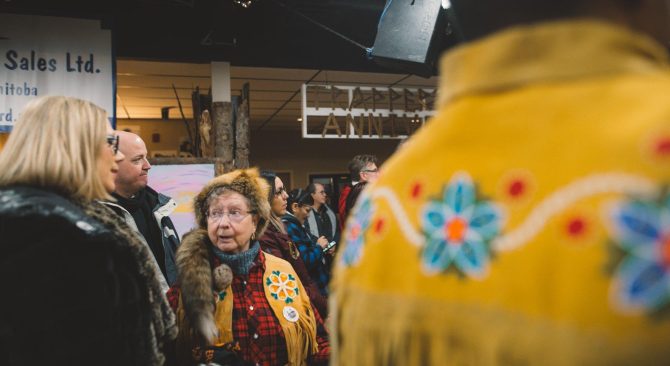 Una persona con chaqueta de cuero con flecos, camisa de cuadros y sombrero de piel se encuentra en el interior de una multitud de personas con vestimenta similar.