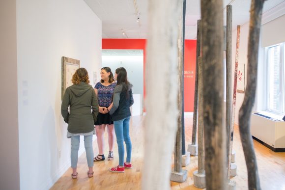 Tres personas observan un cuadro en la pared de una galería de arte.