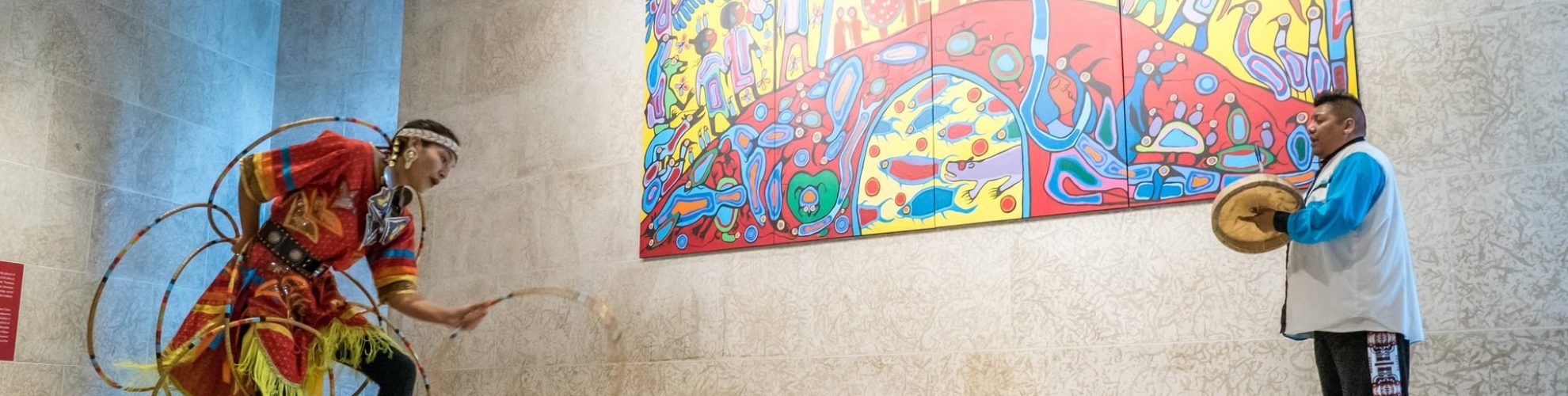 Una persona baila el aro y otra toca el tambor delante de un mural en el WAG.