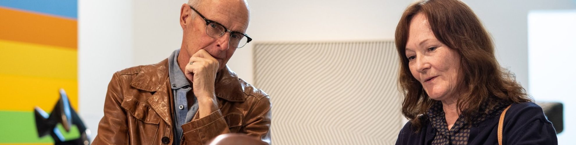 Pareja de ancianos apreciando los intrincados detalles de una escultura de bronce, compartiendo un momento de contemplación/admiración artística.