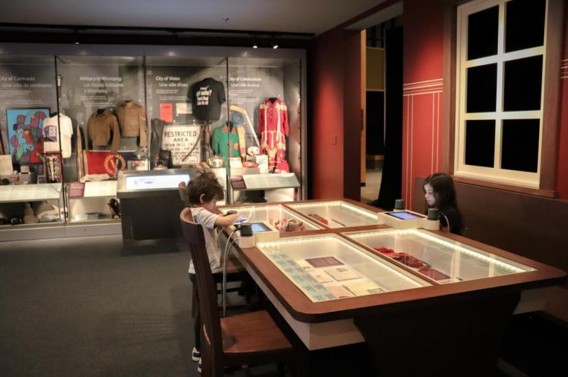 Curious little boy and girl captivated by Winnipeg Museum's finest antiques, peering over the glass showcase box with wonder.