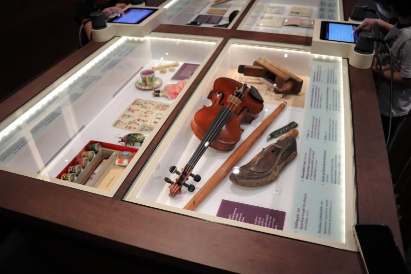 Intricately displayed antique violin steals the spotlight among a collection of assorted artifacts in a glass showcase.