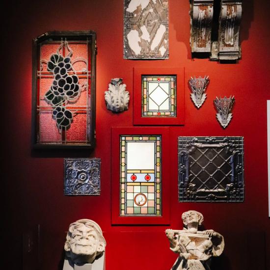 Collection of antique stained glass pieces beautifully arranged on a red wall, casting a kaleidoscope of color and history.