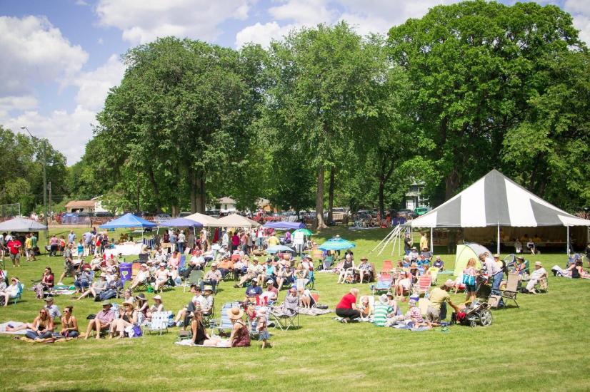 Community gathered on the sunlit grass, immersed in the music and embracing the shared experience with smiles and relaxation.