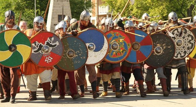 Une rangée de Vikings redoutables, prêts au combat, boucliers levés et le moral au beau fixe, incarnant la détermination d'un guerrier.