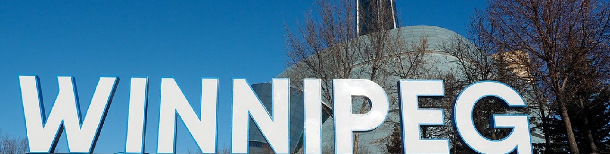 Female standing in front of Winnipeg sign with Canadian Museum for Human Rights in the foreground.