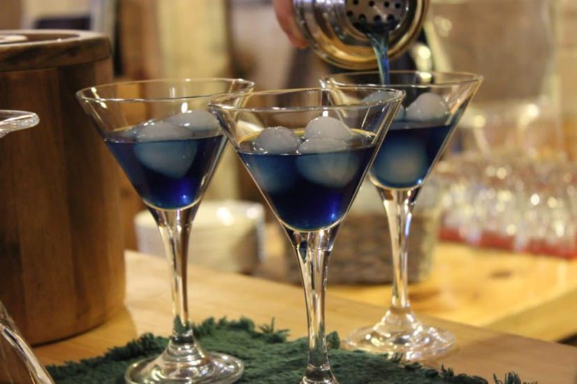 Three royal blue martinis poured from a shaker over ice at the bar, showcasing vibrant cocktails in a lively Manitoba setting