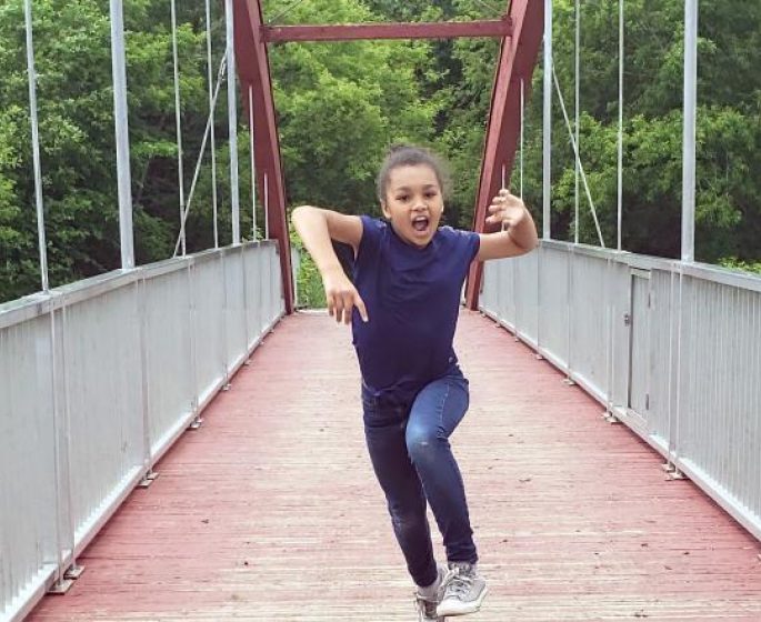 Un enfant danse joyeusement sur un pont, profitant de l'instant présent dans un cadre extérieur magnifique.