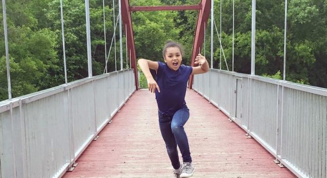 Un enfant danse joyeusement sur un pont, profitant de l'instant présent dans un cadre extérieur magnifique.