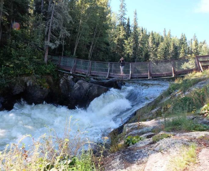 A person standing on the suspension bridge in Wekusko Falls Provincial Park, watching the water rush by.