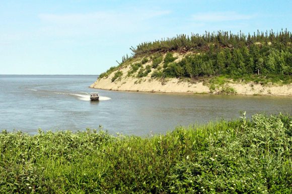 A boat on a lake near a sandy and forested shore, with a clear view of the hillside.