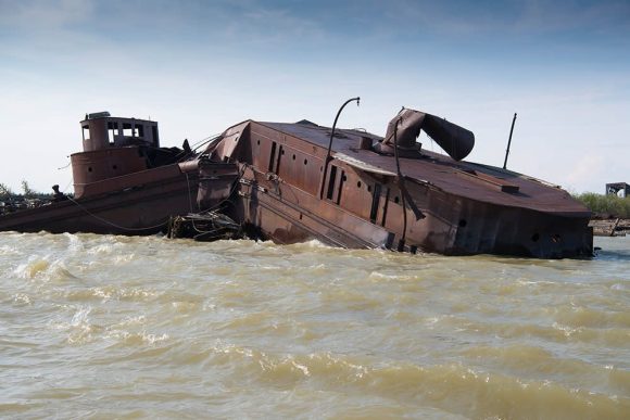 Rustic fur trading boat partially submerged at the water's edge, showcasing natural decay and historical significance.