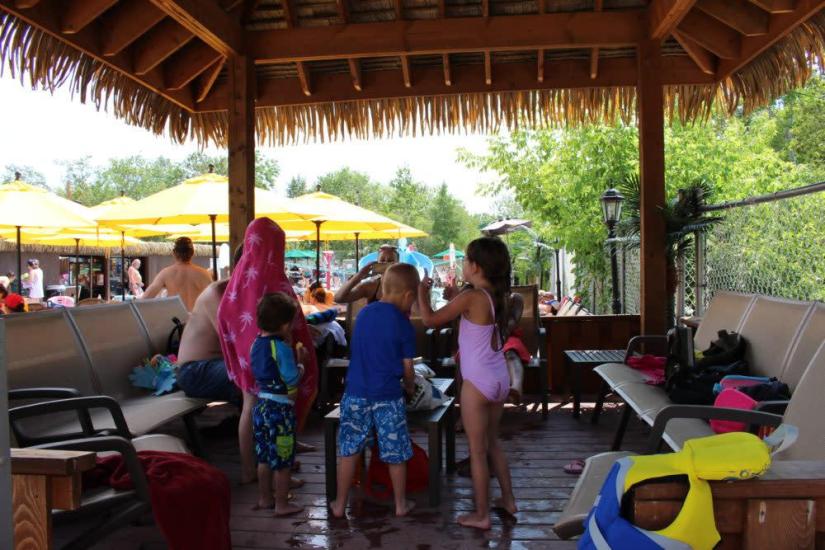 Children gather around a table under a tiki hut, enjoying lunch provided by parents before resuming their water activities.
