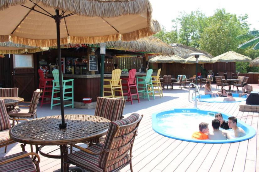 Adults and teenagers relax and chat in hot tubs by the tiki bar at Lilac Resort, enjoying a laid-back atmosphere together.