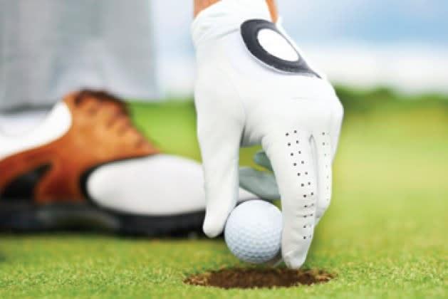Player retrieving ball from Oak Island golf green, showcasing serene golfing amid natural beauty in Manitoba.