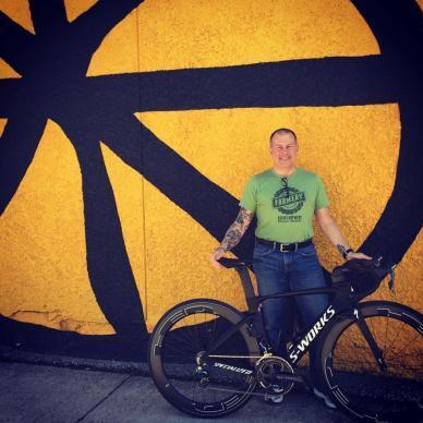 An individual stands outside Woodcock Cycle with their bicycle, ready for adventure in a vibrant outdoor setting.