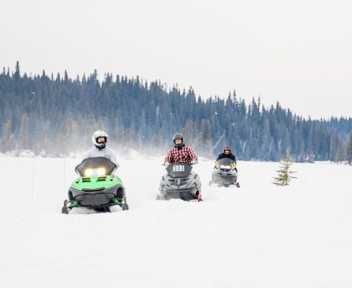 Drei Motorschlittenfahrer fahren in einer Reihe auf einer Piste in Thompson, Manitoba, auf die Kamera zu.