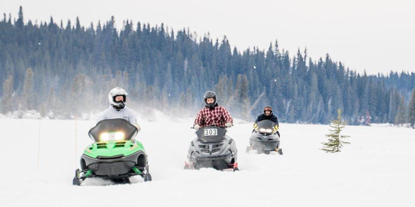 Tres motoristas de nieve cabalgan en fila hacia la cámara en un sendero de Thompson, Manitoba.