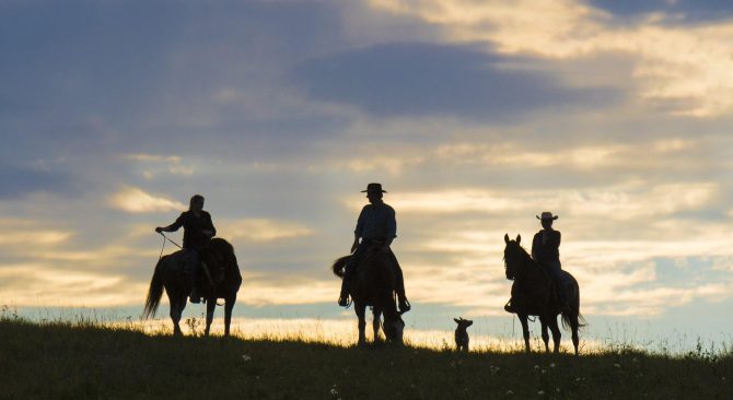 La silueta de tres jinetes se recorta contra el cielo de una pradera.