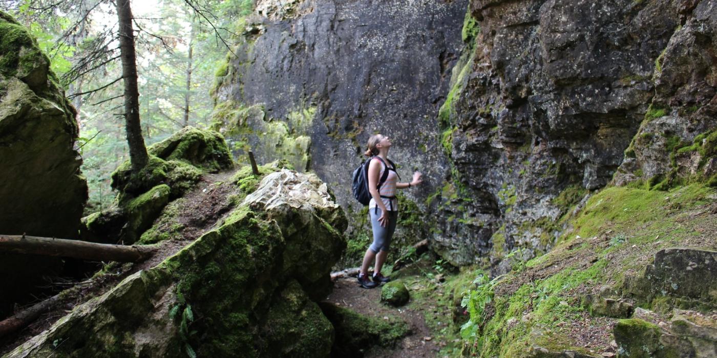 A person looking up a mossy cliff along a hiking trail at Clearwater Lake, The Pas