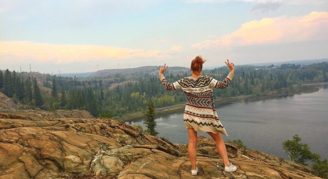 Person posing on rocky hill top overlooking the river near Flin Flon.