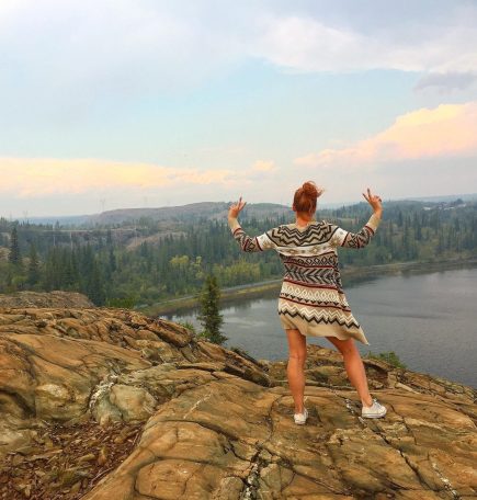Person posing on rocky hill top overlooking the river near Flin Flon.