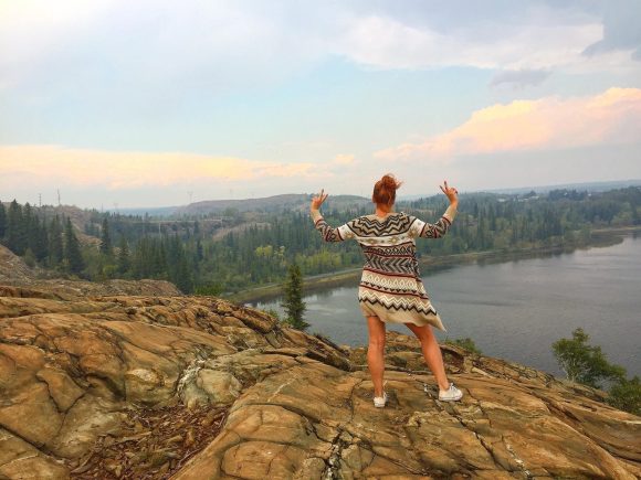 Persona posando en la cima de una colina rocosa con vistas al río cerca de Flin Flon.
