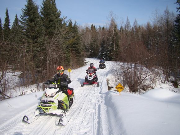 Tres motoristas de nieve en un sendero entre los árboles del Parque Provincial de Nopiming.