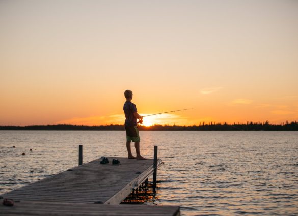 Ein kleines Kind angelt am Ende eines Stegs in The Pas bei Sonnenuntergang.