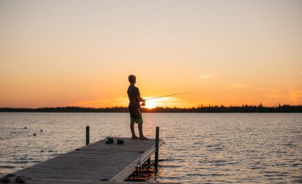 Un niño pescando en el extremo de un muelle en The Pas al atardecer.