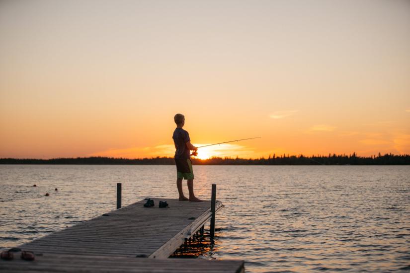 Ein kleines Kind angelt am Ende eines Stegs in The Pas bei Sonnenuntergang.