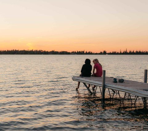 Kinder sitzen am Ende eines Stegs bei Sonnenuntergang in The Pas, Manitoba