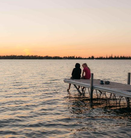 Kinder sitzen am Ende eines Stegs bei Sonnenuntergang in The Pas, Manitoba