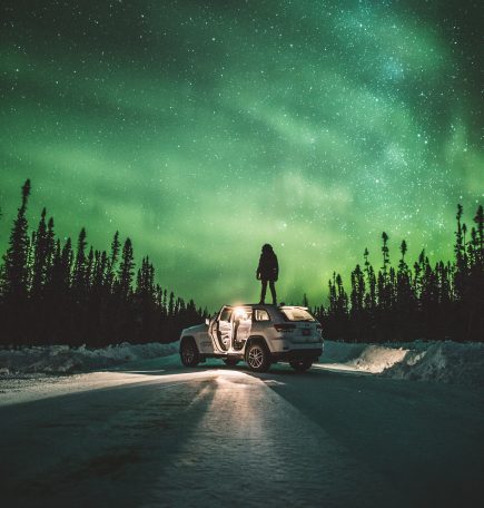 Isang taong nakatayo sa isang kotse na nanonood ng hilagang ilaw sa The Pas