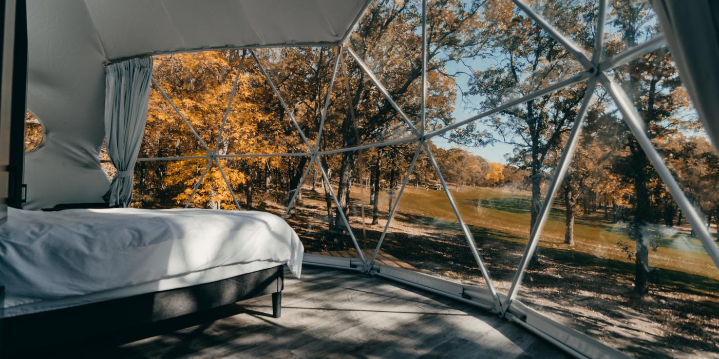 Dans la chambre, il y a un lit et une vue sur le ciel et les arbres.