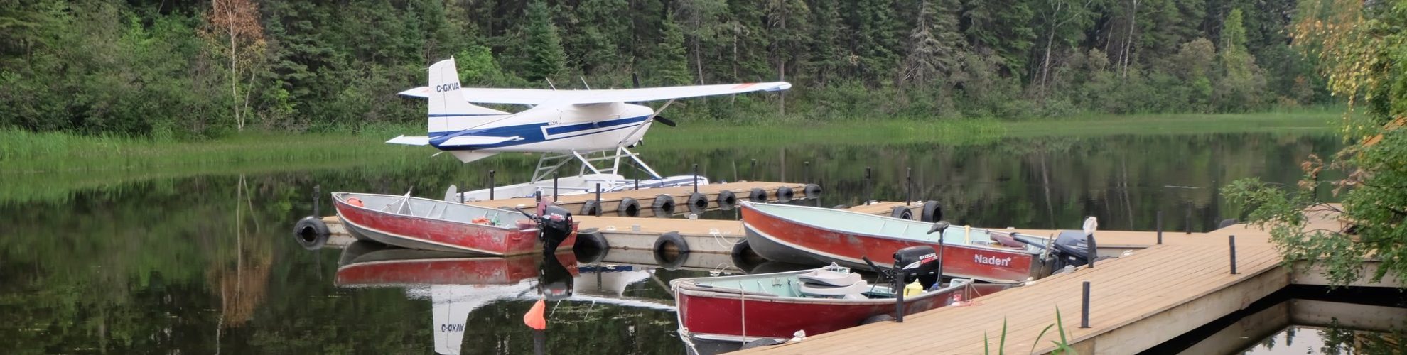 Un hidroavión se posa en un muelle, al que también están amarrados tres barcos de pesca.