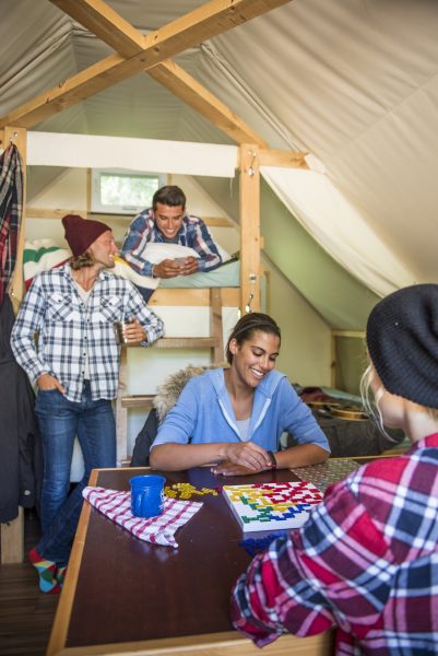 Cuatro jóvenes en el interior de un oTENTik. Dos están sentados a una mesa jugando y otros dos hablan detrás de ellos.