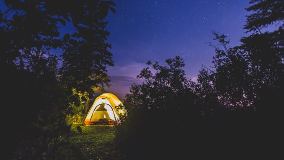 Ein von innen beleuchtetes Zelt leuchtet gegen den dunklen Himmel.