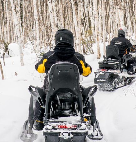 Zwei Personen fahren mit dem Schneemobil durch den Busch in Swan River.
