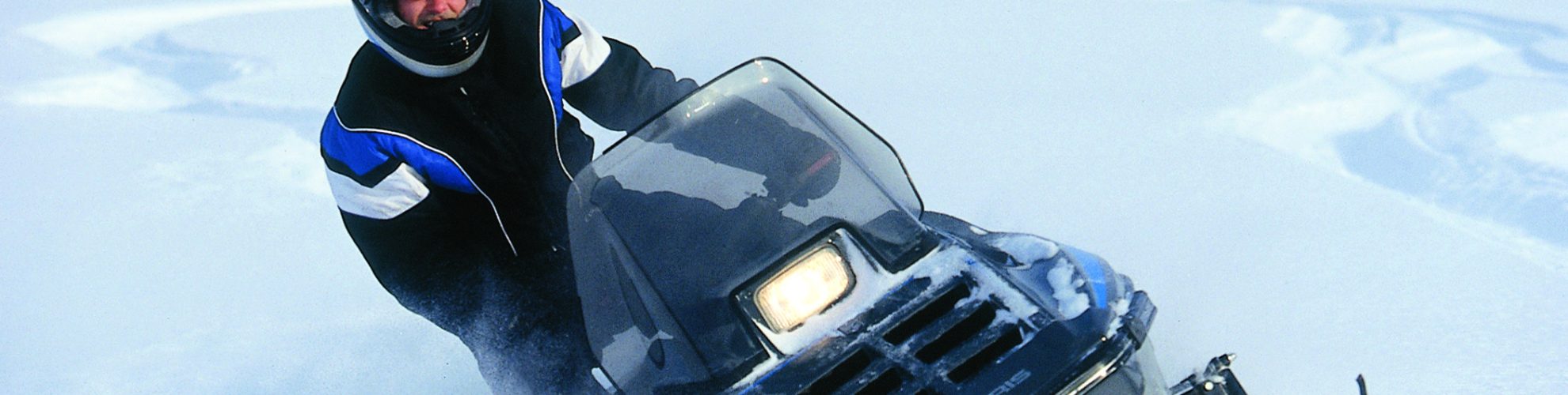 A person on a snowmobile carves a hard banked turn in the deep powder.