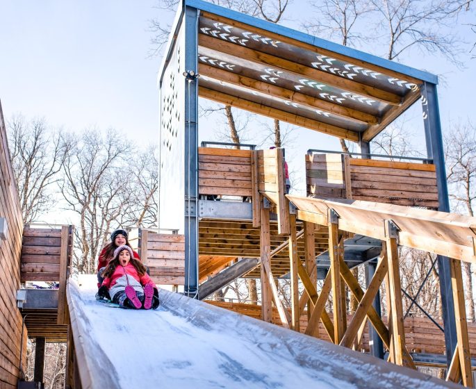 Deux enfants glissant sur une piste de luge en bois.