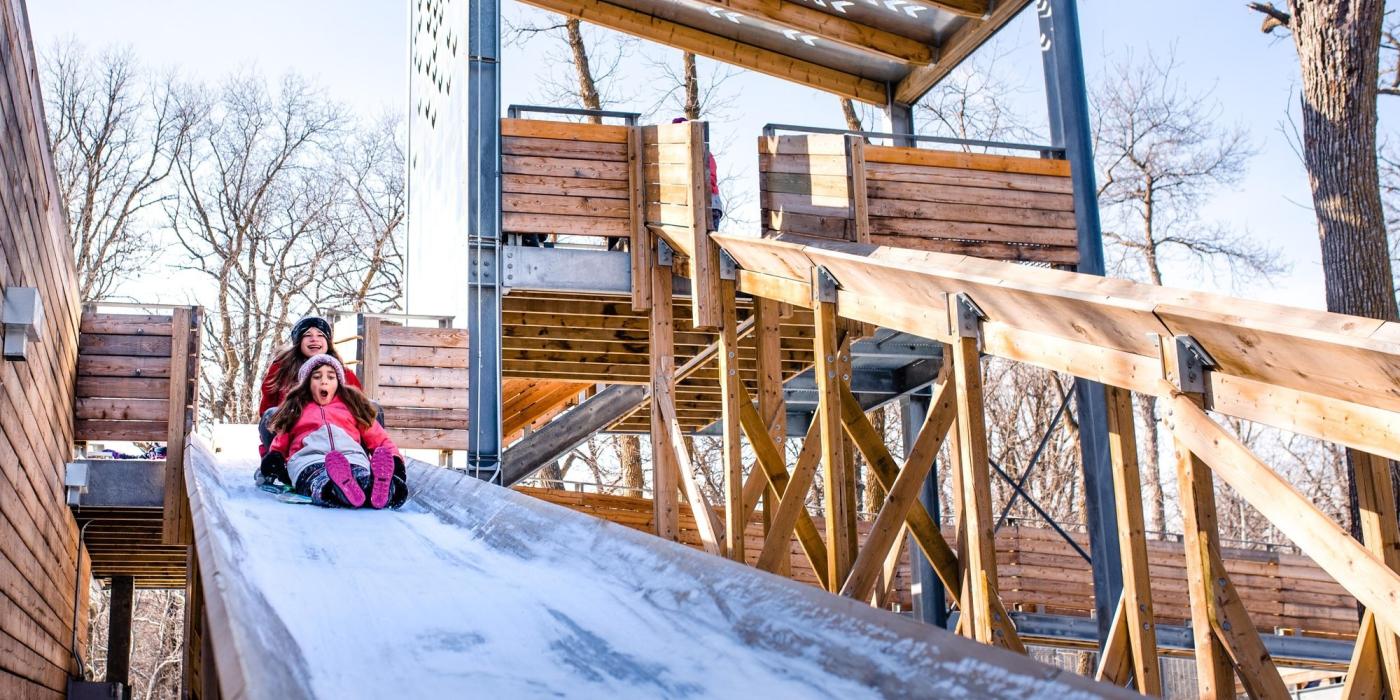 Two children sliding down a wooden toboggan run.