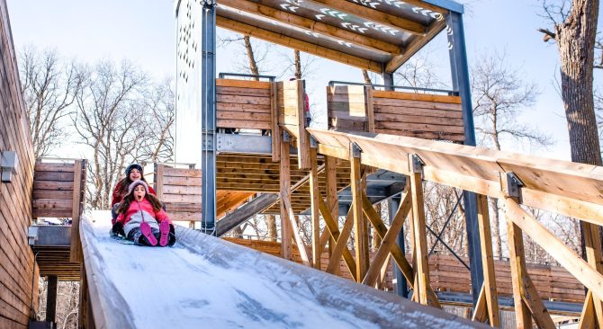 Two children sliding down a wooden toboggan run.