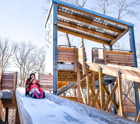 Two children sliding down a wooden toboggan run.