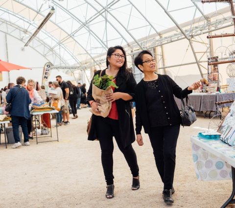 Two people browse St. Norbert Farmer's Market in Winnipeg, one person is carrying a paper bag full of leafy green lettuce.