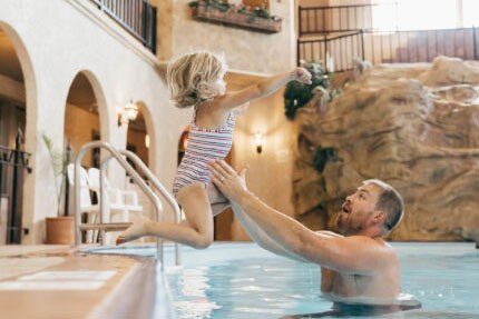 Isang bata na tumatalon sa mga bisig ng kanyang ama sa pool sa Quality Inn sa Morden-Winkler.